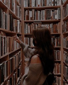 a woman is standing in front of a bookshelf and looking at the shelves