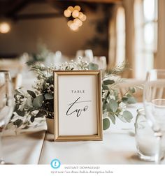 the table numbers are displayed in gold frames on top of white linens and greenery