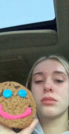 a woman holding up a cookie with a face drawn on it in the back seat of a car