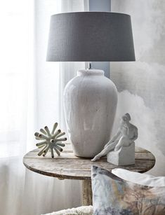 a white vase sitting on top of a wooden table next to a lamp and pillows