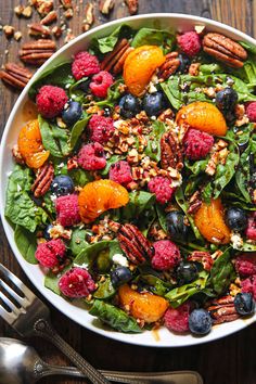 a white bowl filled with spinach, berries and pecans on top of a wooden table