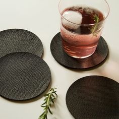 three black coasters and a drink on a white table top with rosemary sprigs