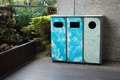 two blue and green trash cans sitting on top of a wooden floor next to plants