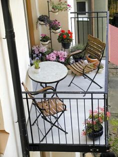 two chairs and a table on a balcony with potted flowers in the corner next to them