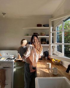 a woman and child are in the kitchen looking out the window at the trees outside