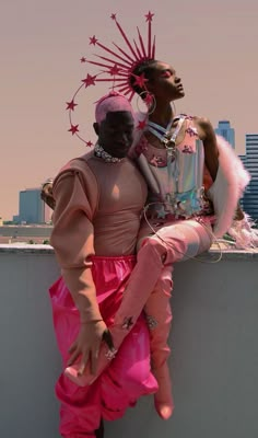 two people sitting on top of a wall next to each other wearing pink outfits and headgear