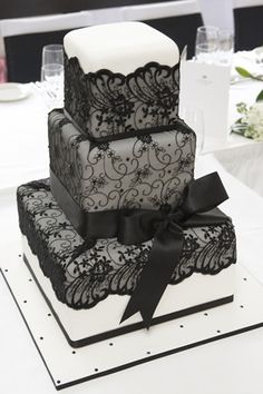 a three tiered cake with black lace and bows on the top is sitting on a table