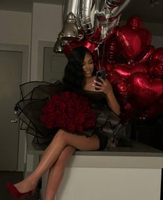 a woman sitting on top of a counter next to red roses and balloons in the shape of hearts