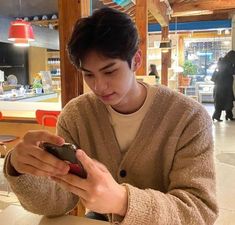 a young man sitting at a table looking at his cell phone while holding it in his hand