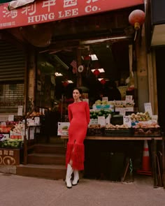 a woman standing in front of a store wearing a red dress and white booties