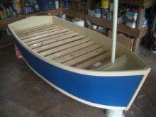 a blue and white boat sitting on top of a wooden floor in a room filled with shelves