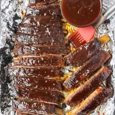 bbq ribs and barbecue sauce on tin foil with tongs next to the grill