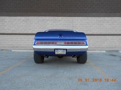 the back end of a blue car parked in a parking lot next to a brick wall