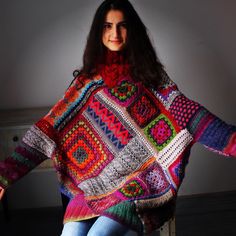 a woman is sitting on a chair wearing a colorful crocheted ponchle