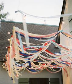 an outdoor party with streamers, lights and decorations hanging from the ceiling in front of a house