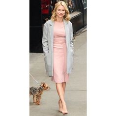 a woman in a pink dress and coat walks her dog down the street on a leash