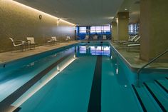 an indoor swimming pool with lounge chairs and lights on the side wall next to it