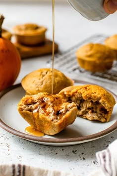 someone is pouring syrup on some muffins that are sitting on a white plate