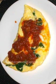 an omelet with tomato sauce and spinach leaves on it is sitting on a white plate