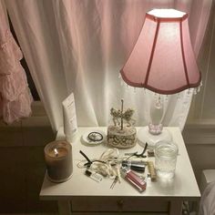 a white table topped with a lamp next to a pink shade on a window sill