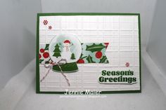 a christmas card with a snowman and holly tree on it, sitting on a white surface