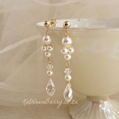 a pair of pearls and gold earrings on a white pedestal with a veil in the background