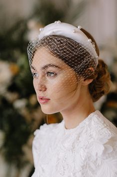 a woman with a veil on her head is wearing a white dress and looking off to the side