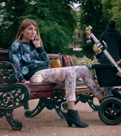 a woman sitting on a bench talking on her cell phone while holding a stroller