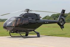 a black helicopter sitting on top of a tarmac next to a lush green field