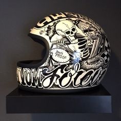 a motorcycle helmet is displayed on a black shelf in front of a gray wall with the words moto's and skulls written all over it