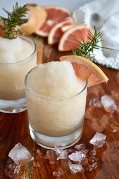 two glasses filled with ice and grapefruit on top of a wooden cutting board