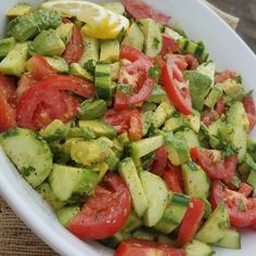 a white bowl filled with cucumber, tomatoes and other veggies on top of a wooden table