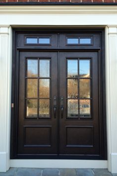 a black double door with two sidelights in front of a brick wall and white trim