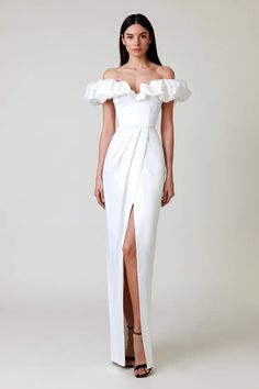 a woman wearing a white dress with an off the shoulder ruffled top and thigh high slit