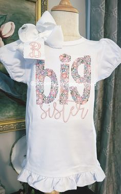 a white t - shirt with the word big sister printed on it and a bow at the neck