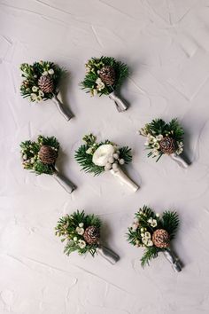 wedding boutonnieres with pine cones, flowers and greenery on a white surface