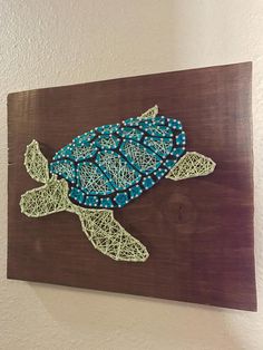 a string art turtle on a wooden board with blue and green beads in its shell