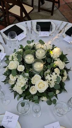 a white table topped with lots of glasses and plates covered in flowers next to candles