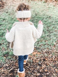 a little boy walking in the woods wearing a knitted sweater and ear warmers