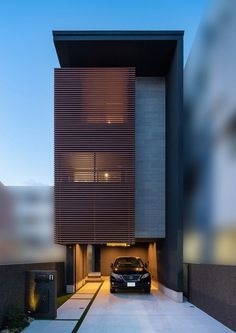 a car is parked in front of a modern house at dusk with its lights on