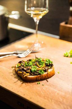 a wooden cutting board topped with a pizza covered in toppings next to a glass of wine