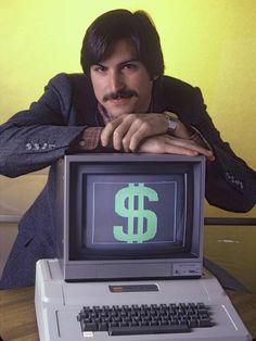 a man leaning over an old computer with a dollar sign on it