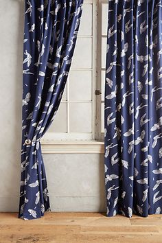 a blue curtain with birds on it in front of a white wall and wooden floor