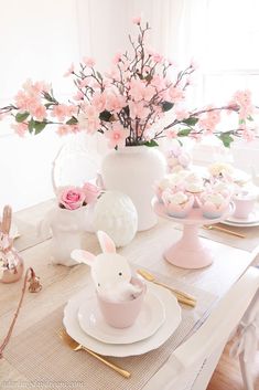 a table set for easter with pink flowers and bunny ears on the placemats