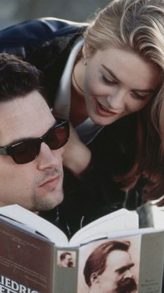 a man reading a book to a woman with sunglasses on her head while leaning over him