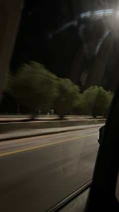 a car driving down a street at night time with the lights on and trees in the background