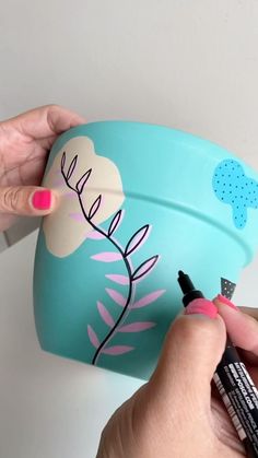 a woman is painting the inside of a cup with pink and blue flowers on it