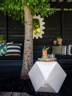 a white table sitting next to a tree on top of a wooden floor covered in pillows