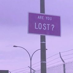 a purple sign that says are you lost? on a pole next to a fence