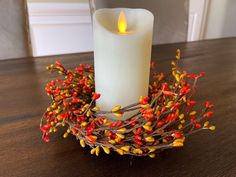 a lit candle sitting on top of a wooden table next to a twig wreath